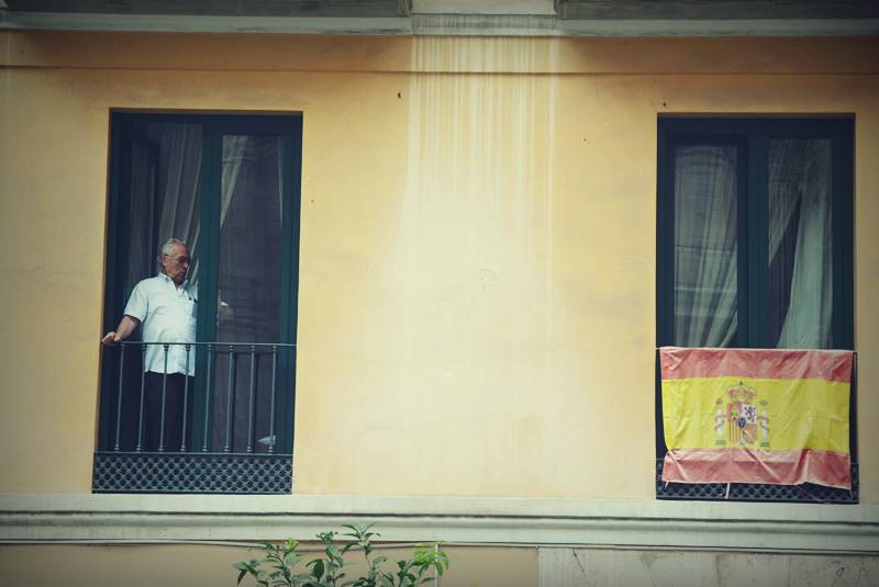 Persona en un balcón junto a la bandera de España.